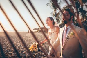 Couple walking along a beach at sunset with palm trees and flowers.
