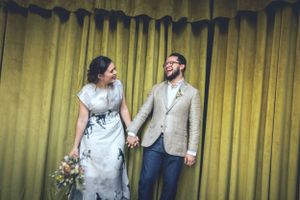 Couple standing together in front of yellow curtains during a casual wedding ceremony.