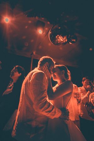 A romantic couple dancing under red mood lighting and disco balls at a party.