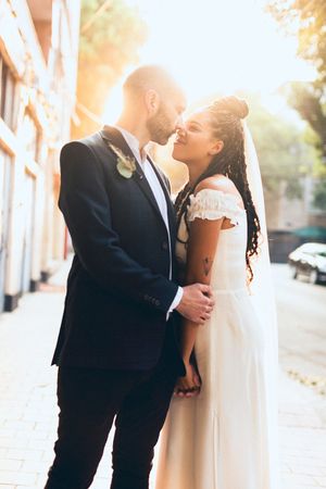 Romantic wedding portrait of couple embracing in warm sunlight against urban backdrop.