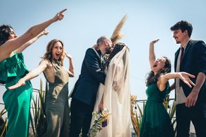 Wedding party celebrating with energetic poses against blue sky.