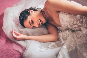 Bride in lace gown laying on pink carpet during wedding day preparation.