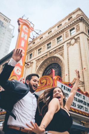 Joyful couple celebrating outside historic theater with bright marquee sign.