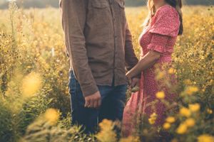 Couple standing in sunlit field of yellow wildflowers at golden hour.