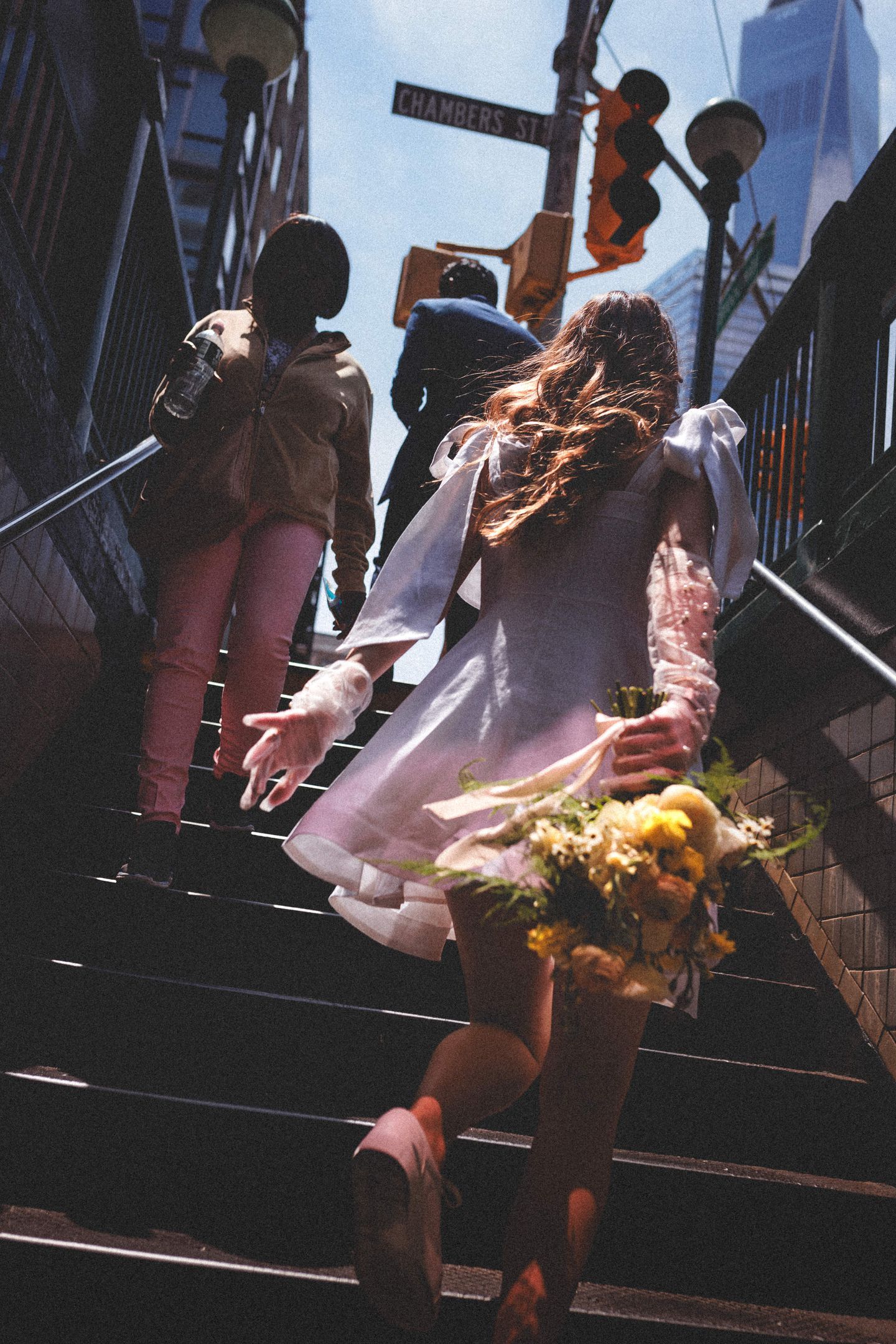 A person carrying flowers while walking up urban steps with wind-blown hair.