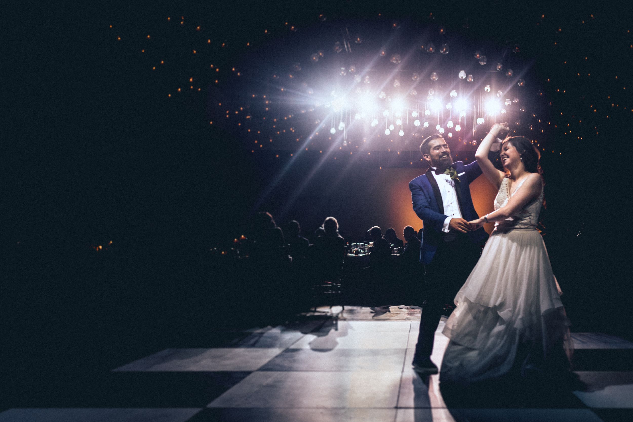 A bride and groom share an elegant dance under dramatic spotlights on their wedding day.