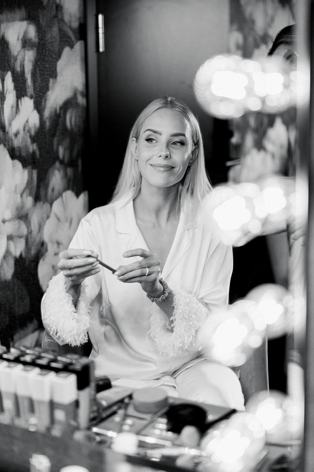 A black and white photo series showing someone in a white robe applying makeup at a vanity mirror.