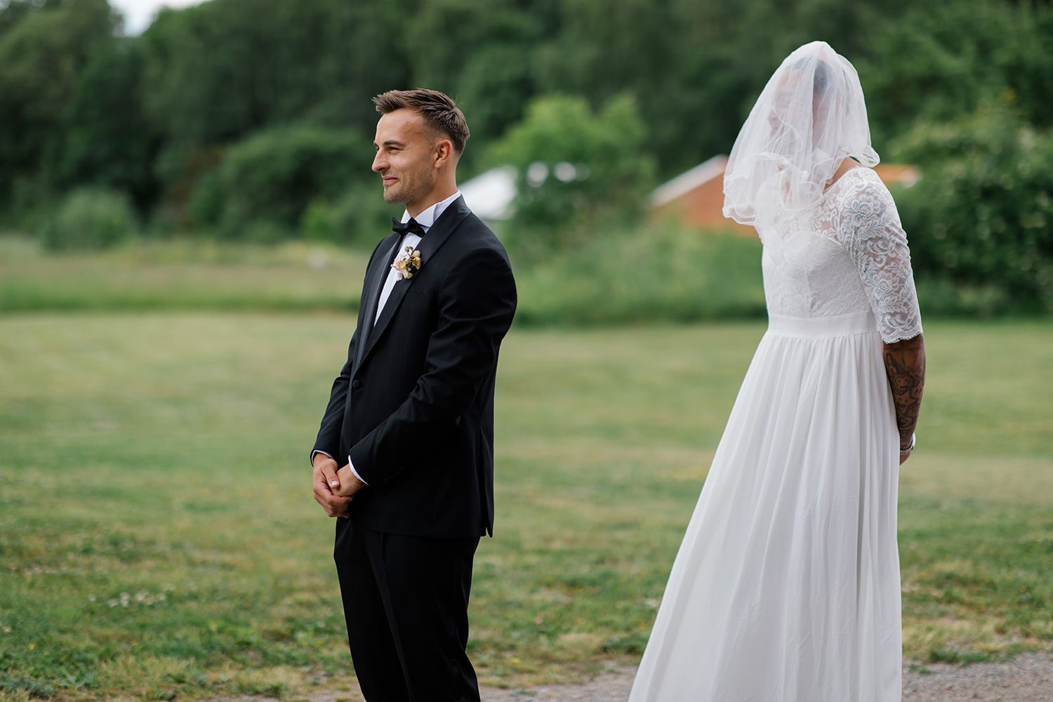 A bride and groom stand together in a lush green field during their outdoor wedding celebration.