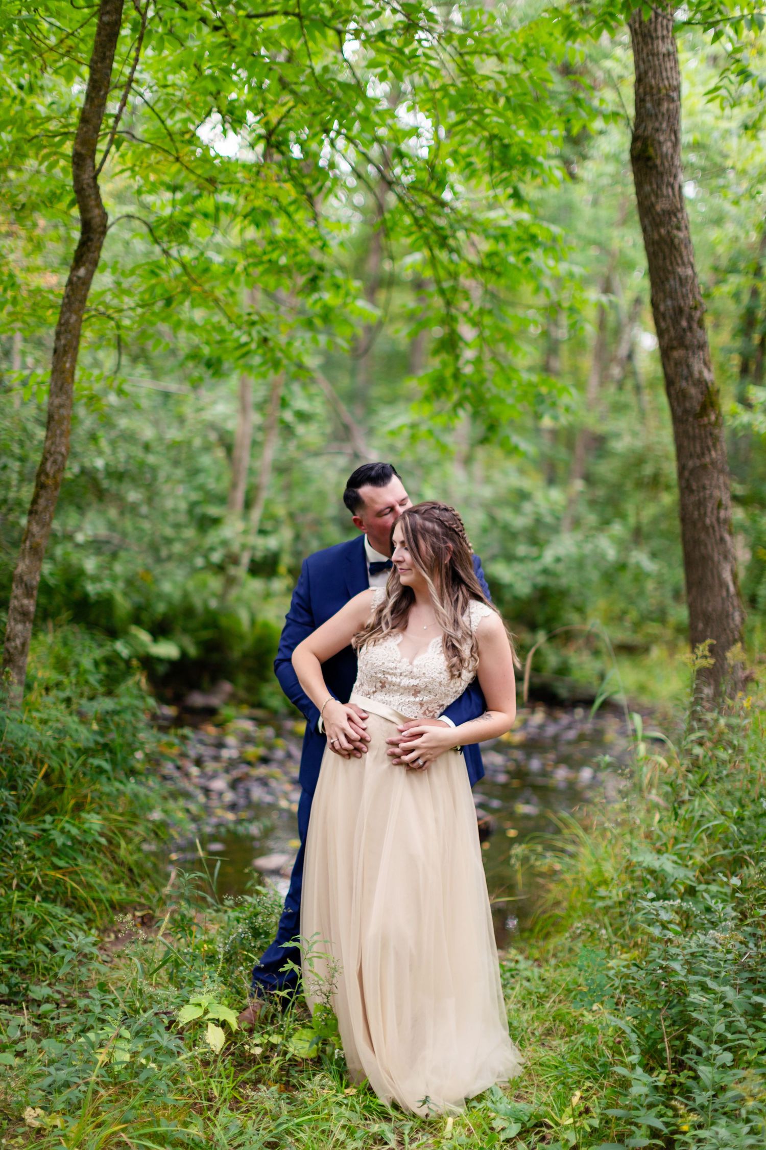 A Bride and Groom share an intimate moment together in a lush green forest setting during their wedding day