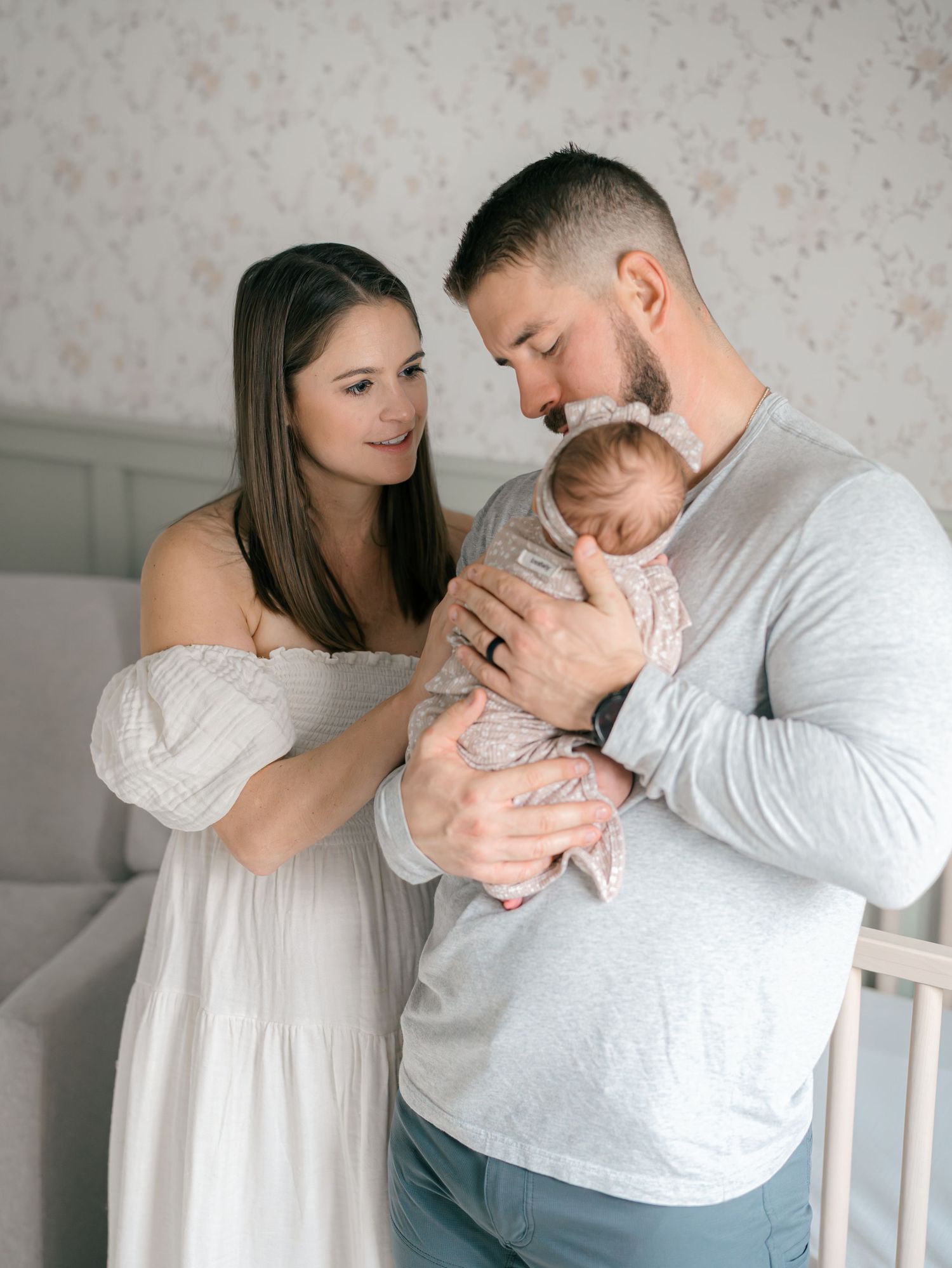 New parents hold her newborn baby in the nursery in front of a sage wall.