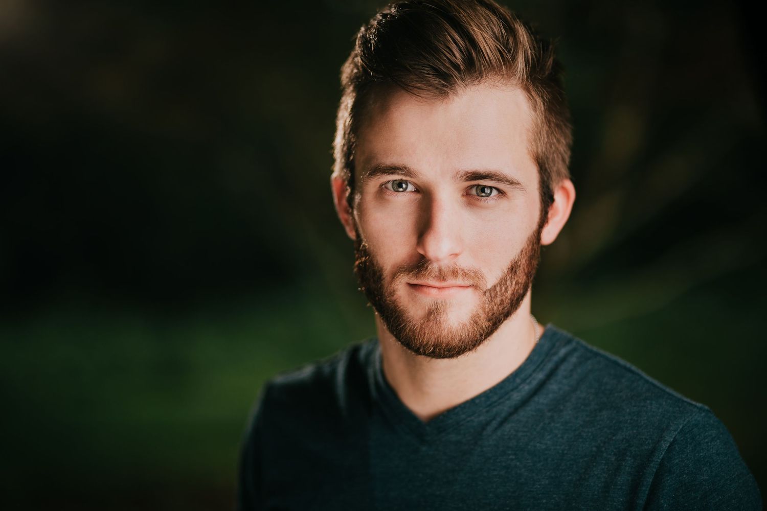 Professional portrait photography with dark background and natural lighting in an outdoor setting.