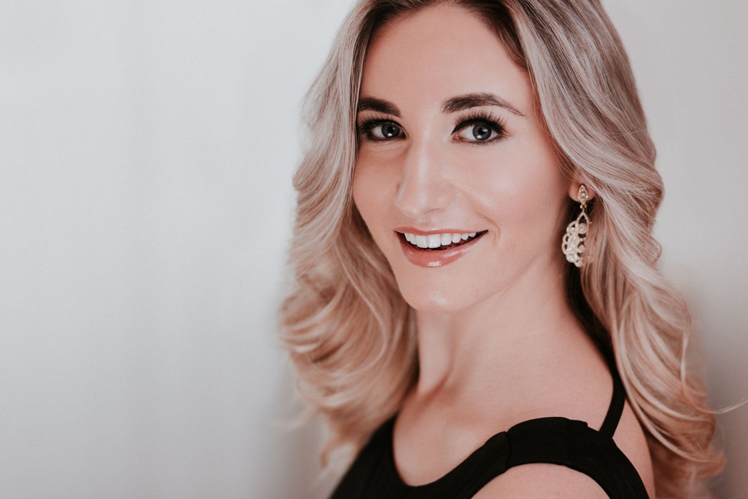 Professional headshot photo series of a woman with blonde hair wearing a black top and smiling against a light background.