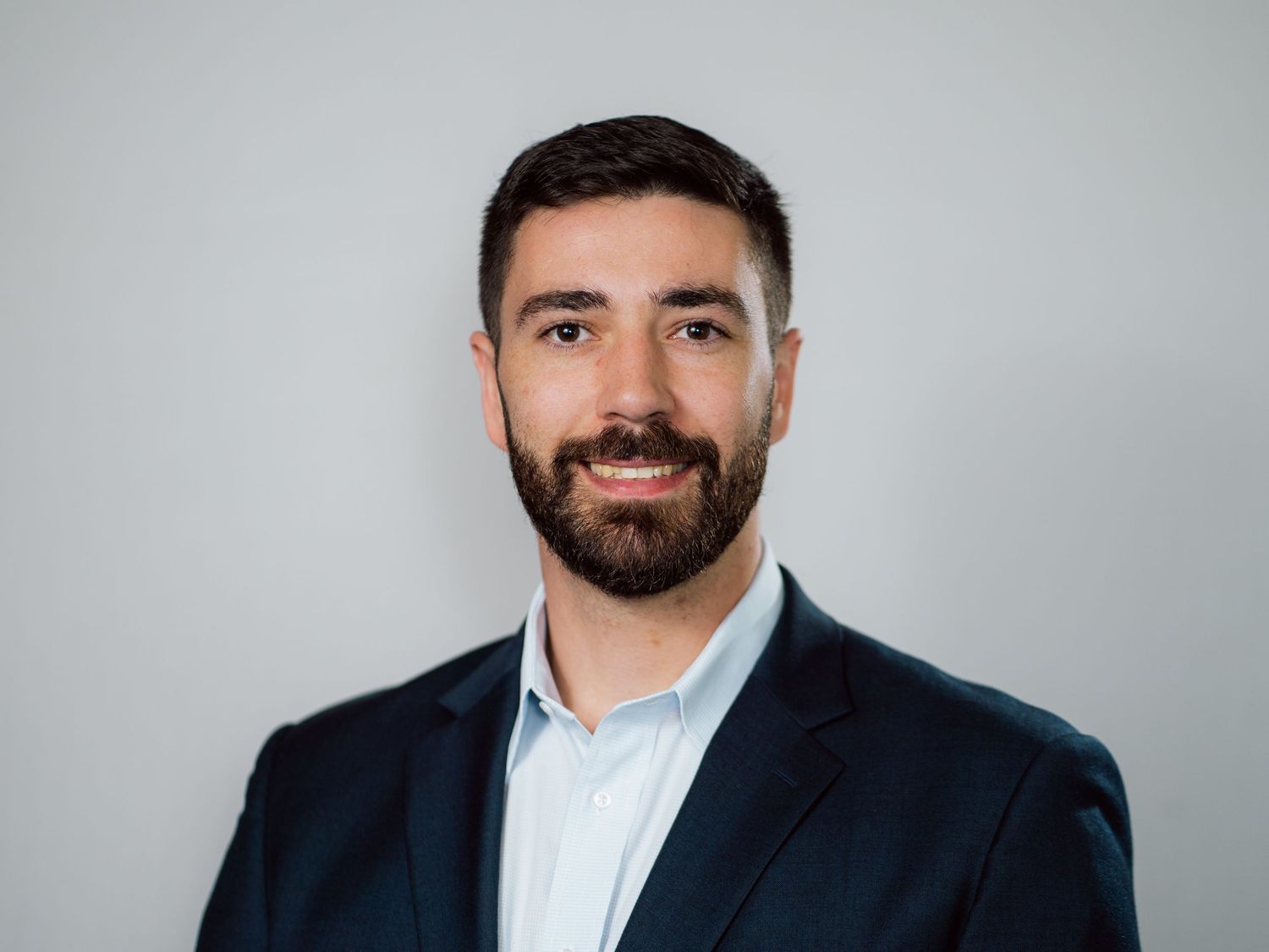 Professional headshot portraits of a person in business attire against a light gray background.