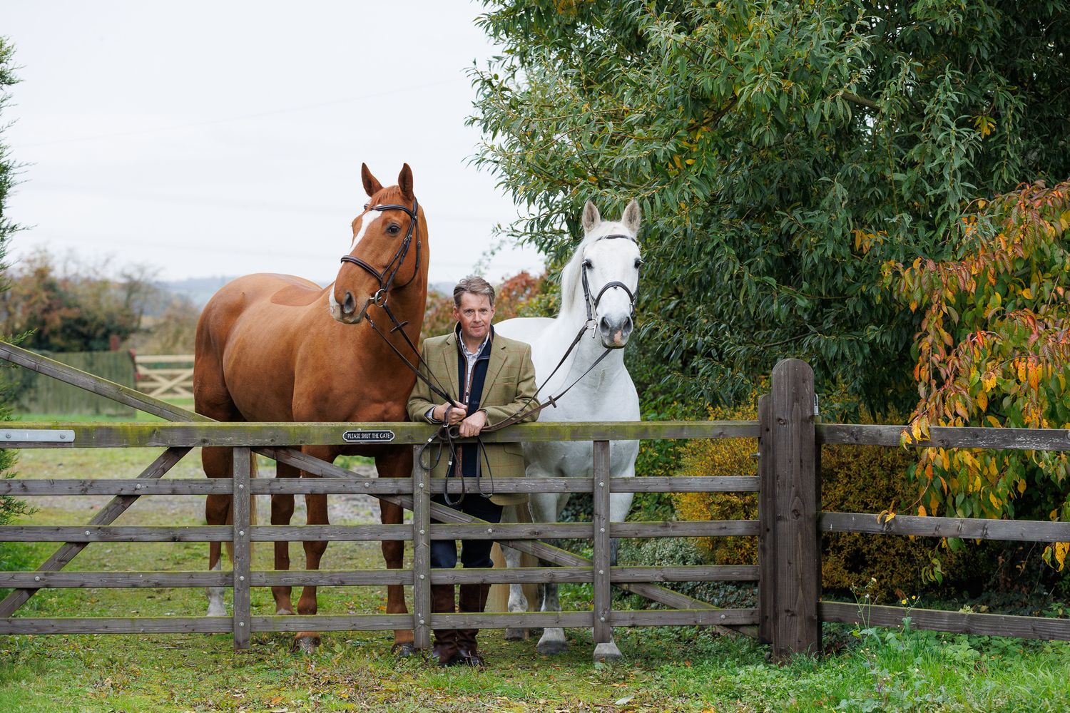 Two riders stand with their animals - a dog and a dark horse relaxing outdoors in a black and white photo.