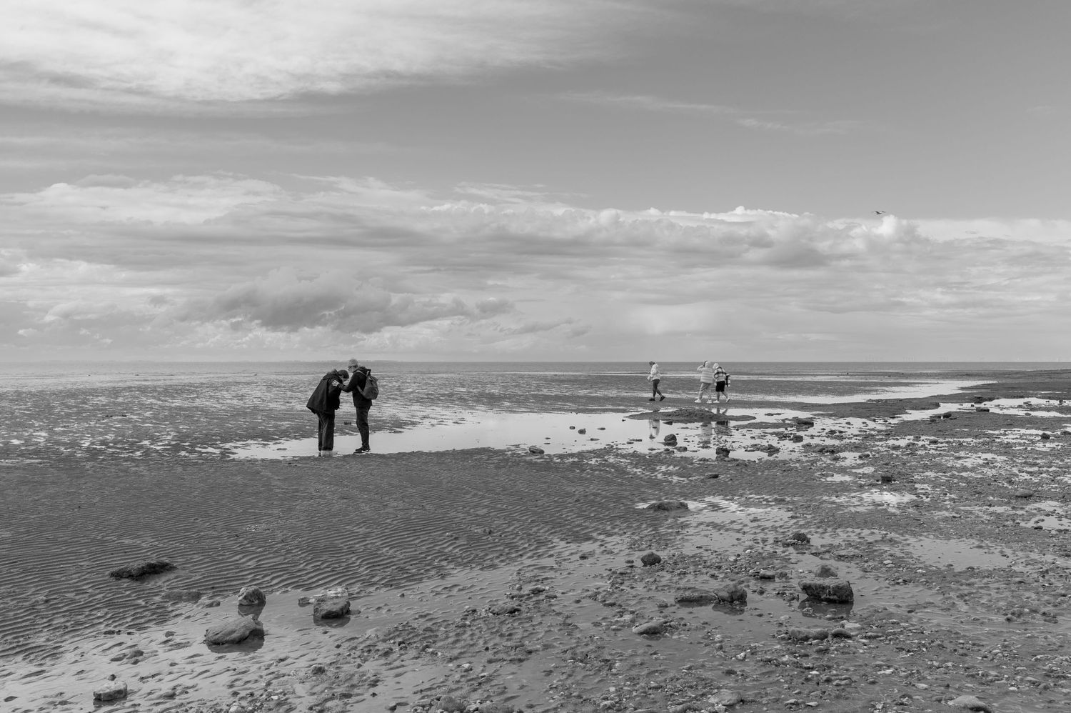 Silhouetted figures stand on a rocky overlook with dramatic cloudy skies and coastal views stretching to the horizon.