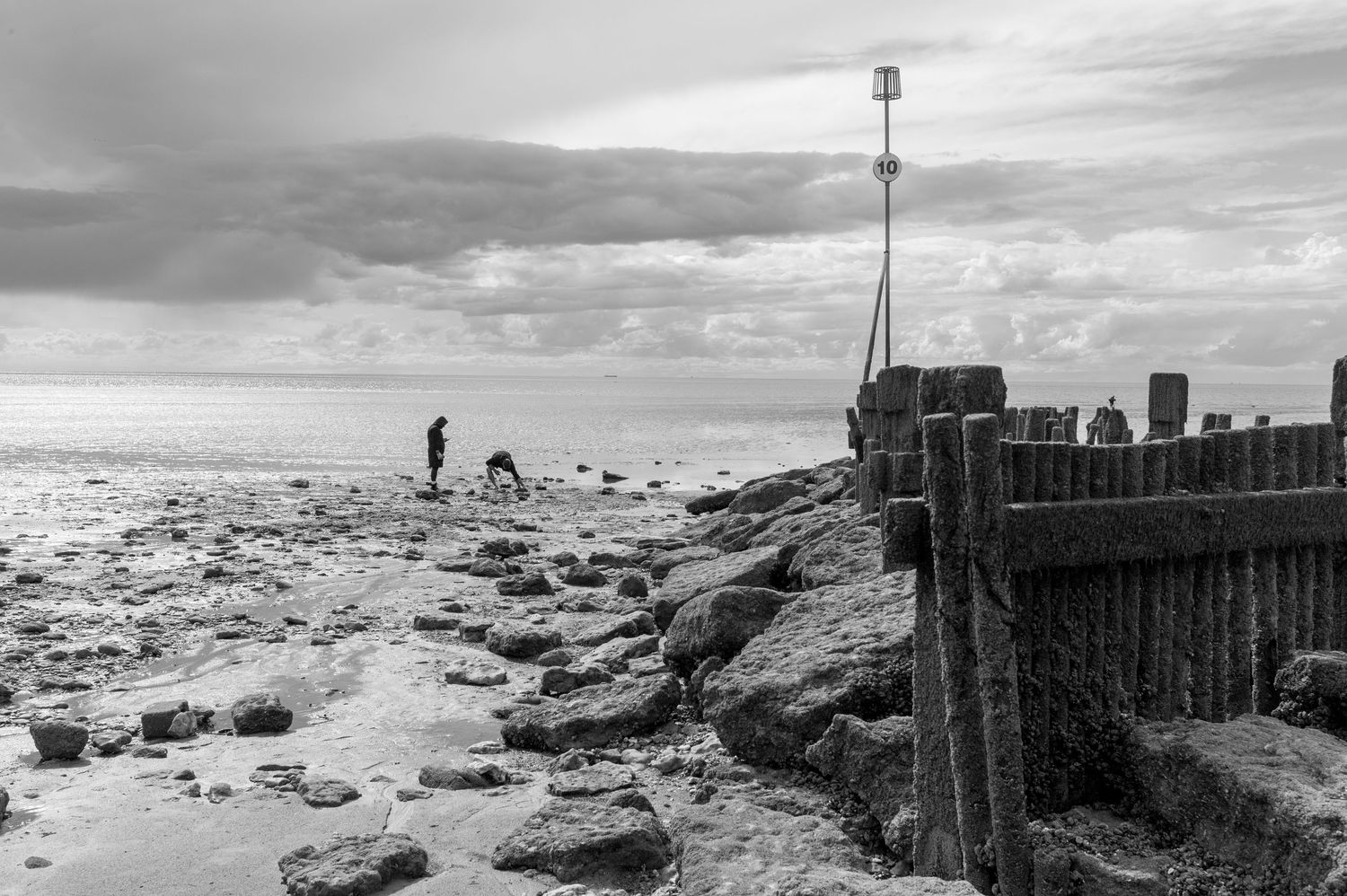 A series of black and white photographs showing a wooden pier extending into a rocky beach at different angles and times.
