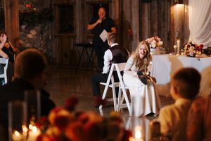Guests mingle and dance at an elegant rustic wedding reception with warm lighting and white chairs.