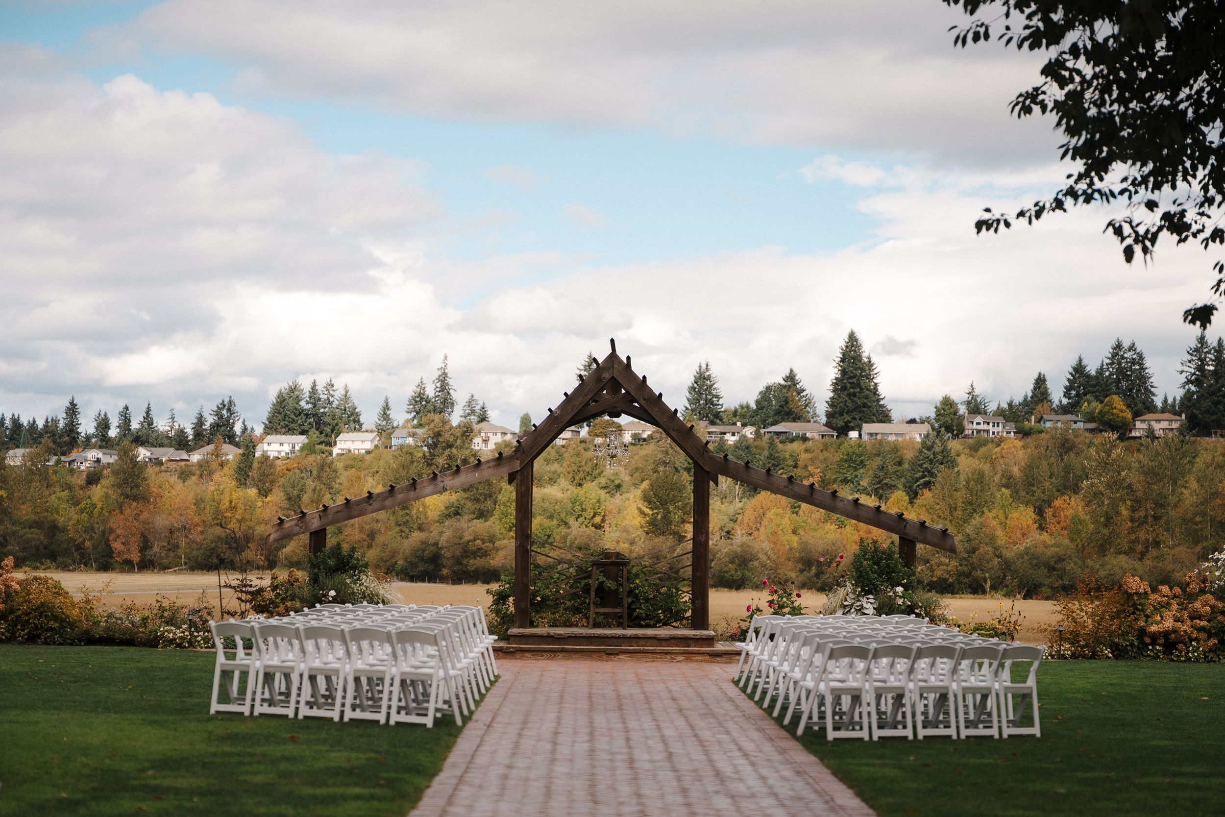White chairs line both sides of an outdoor wedding ceremony aisle with mountain and forest views in the background.