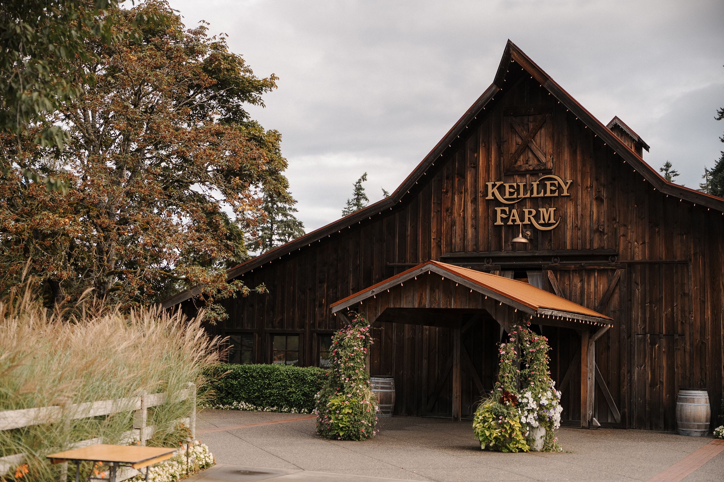 A rustic wooden barn with fall foliage and cloudy skies creates a charming countryside scene.