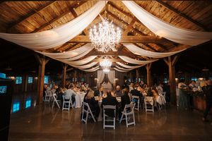 A rustic barn wedding reception venue decorated with elegant white draping and crystal chandeliers.