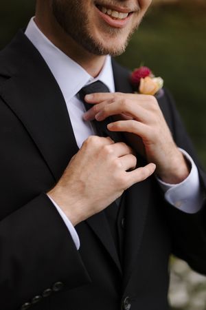 A series of close-up shots showing hands adjusting a black tie and boutonniere on a formal suit.