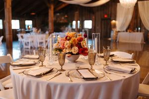 Elegant wedding reception table setting with white linens, champagne glasses and vibrant orange and pink floral centerpiece.