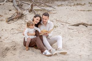 jong gezin tijdens een fotoshoot, zittend in het zand en kijken samen in een boek