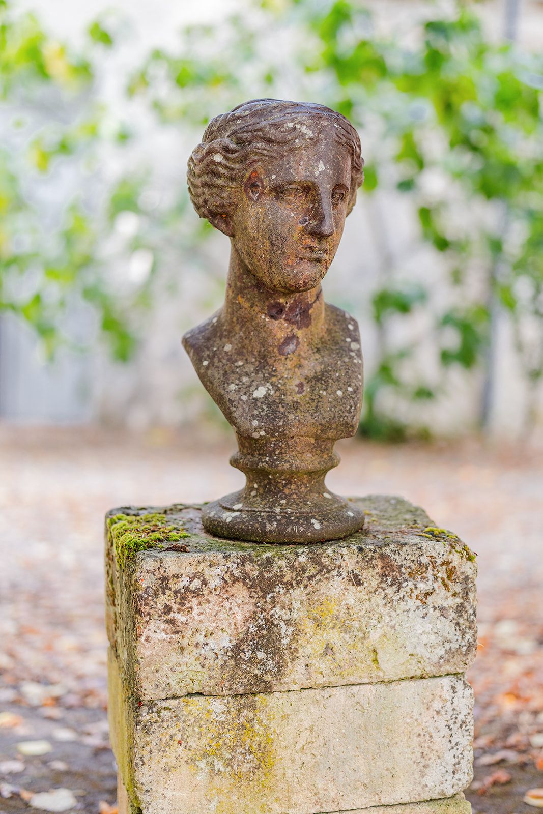 Close-up view of weathered stone garden sculptures showing classical busts covered in moss and patina.