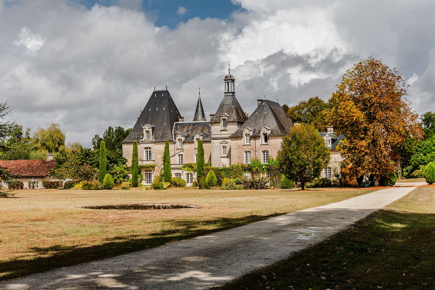 A panoramic view of a historic chateau estate in France with autumn trees and cloudy skies.