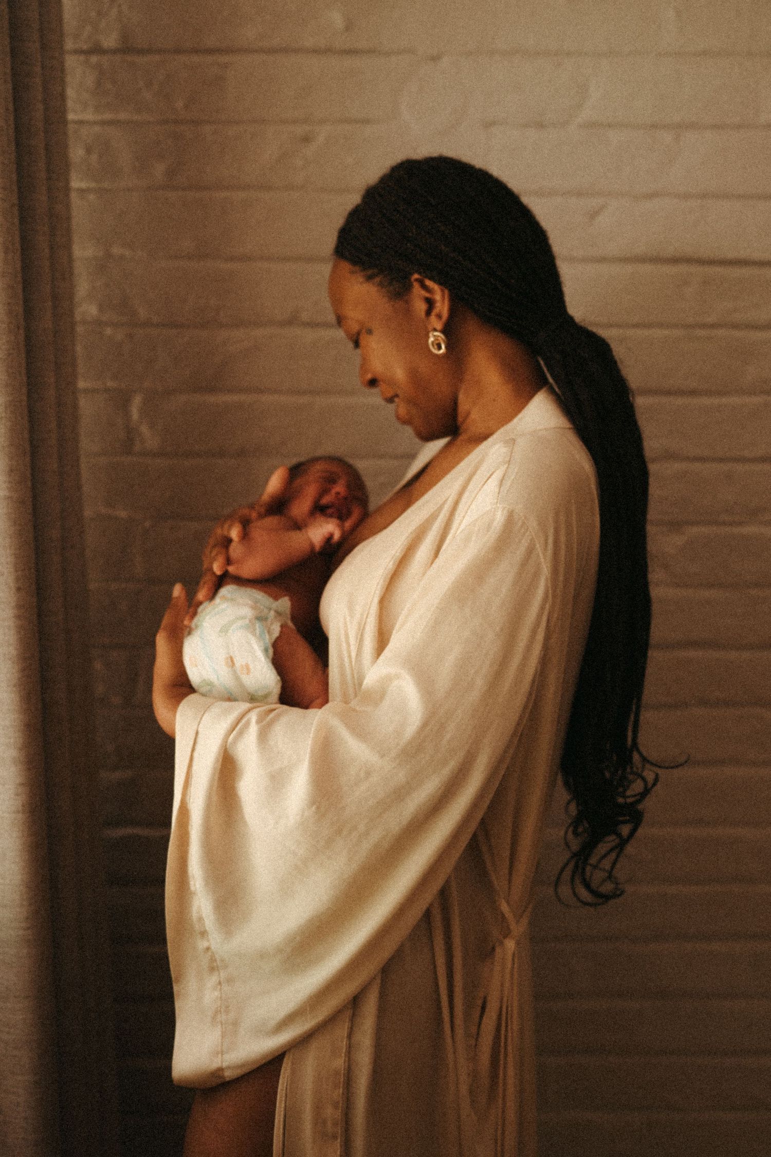 A tender moment captured in warm tones as a mother cradles and kisses her newborn baby.