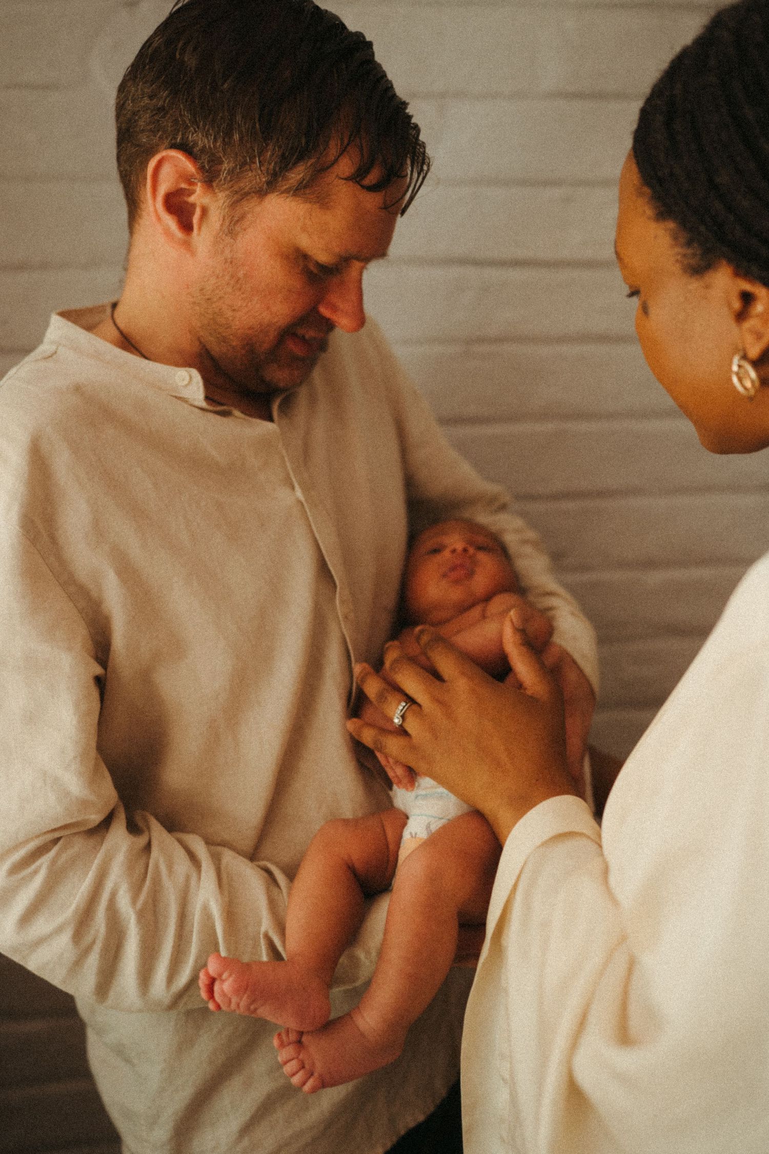 Parents in white clothing share tender moments with their newborn baby.