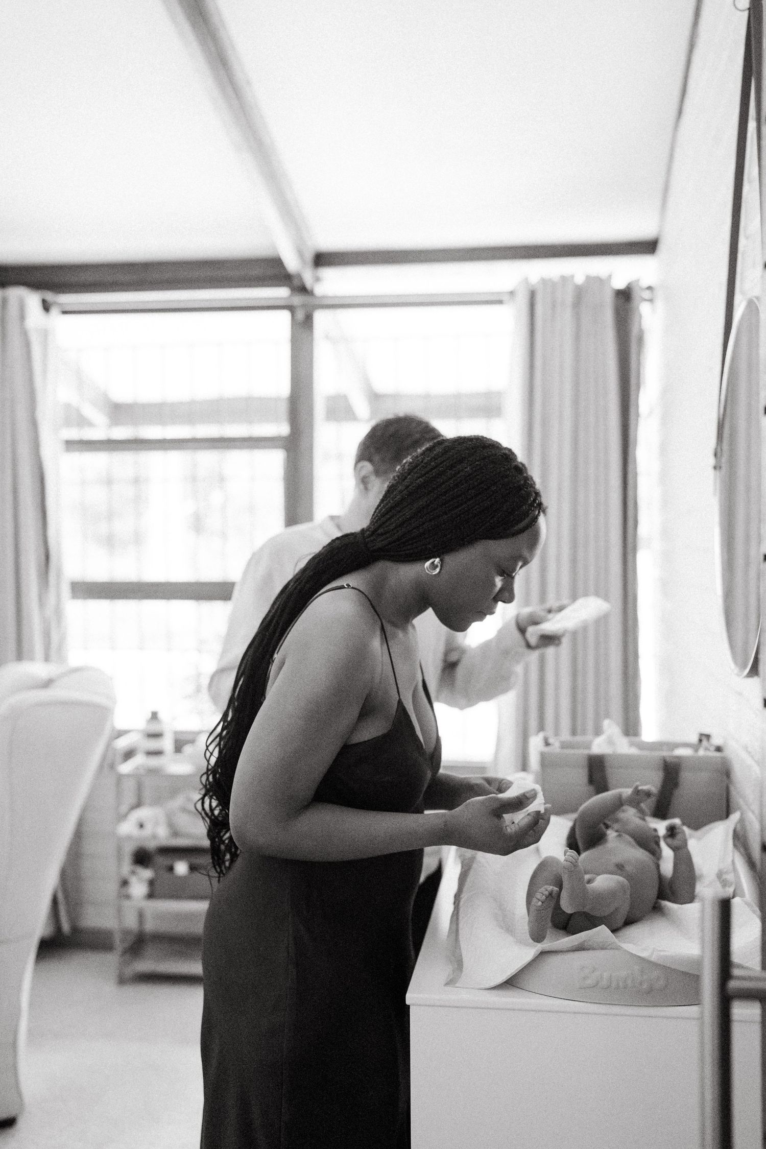 Black and white photos showing quiet moments of newborn care in a bright room.