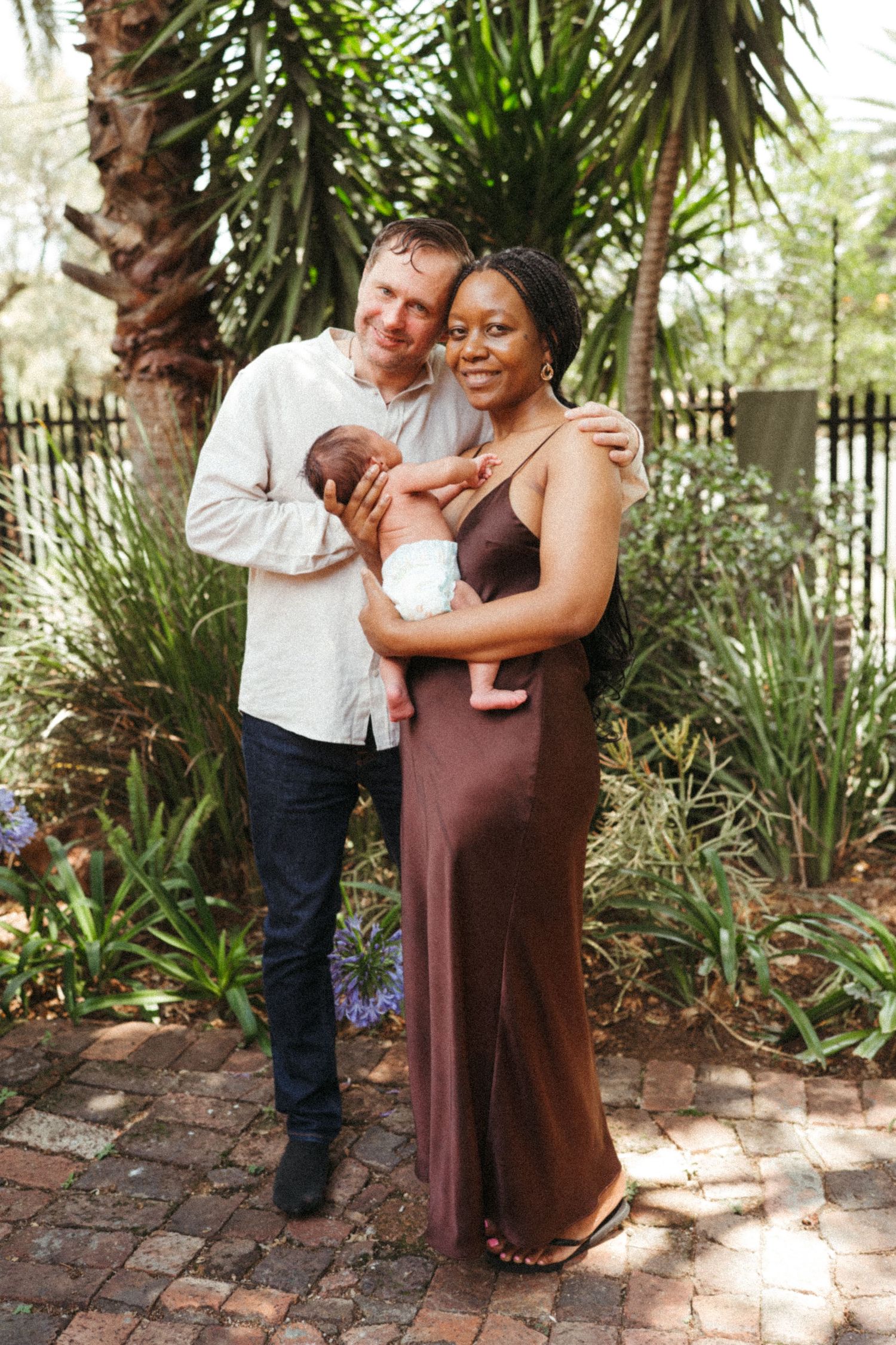 A family poses together outdoors among tropical plants and palm trees.