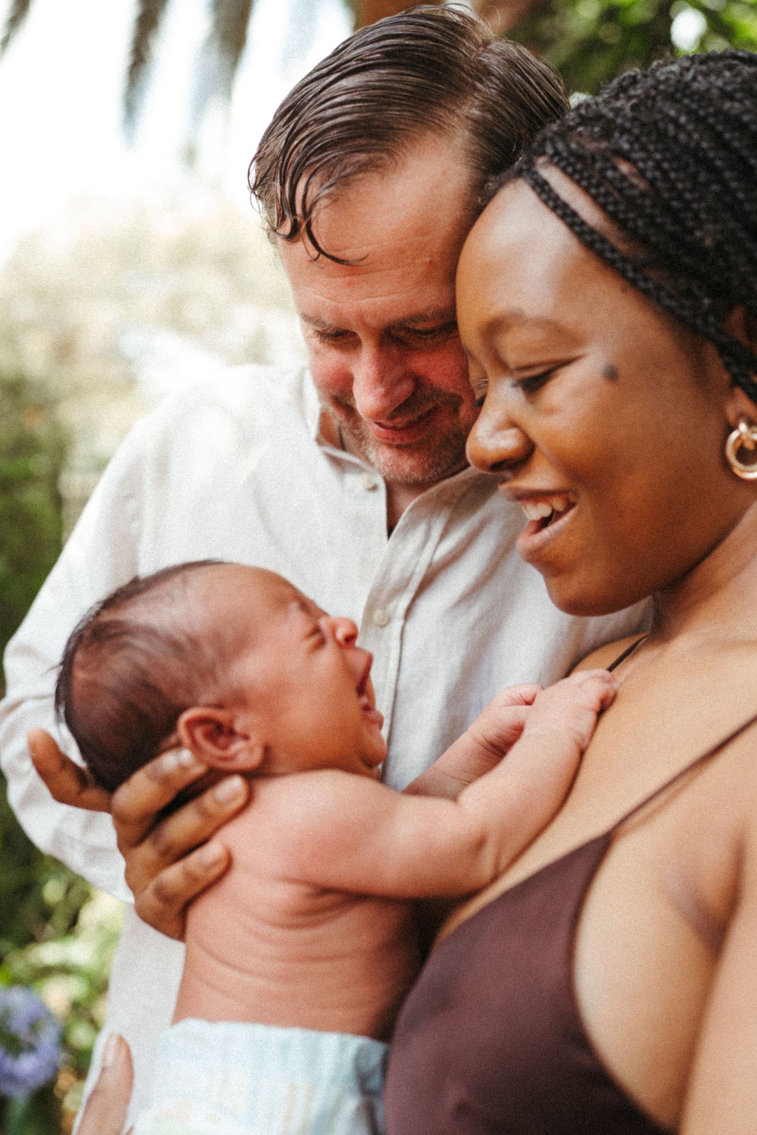 Parents share loving moments with their newborn baby in a sunny outdoor setting.