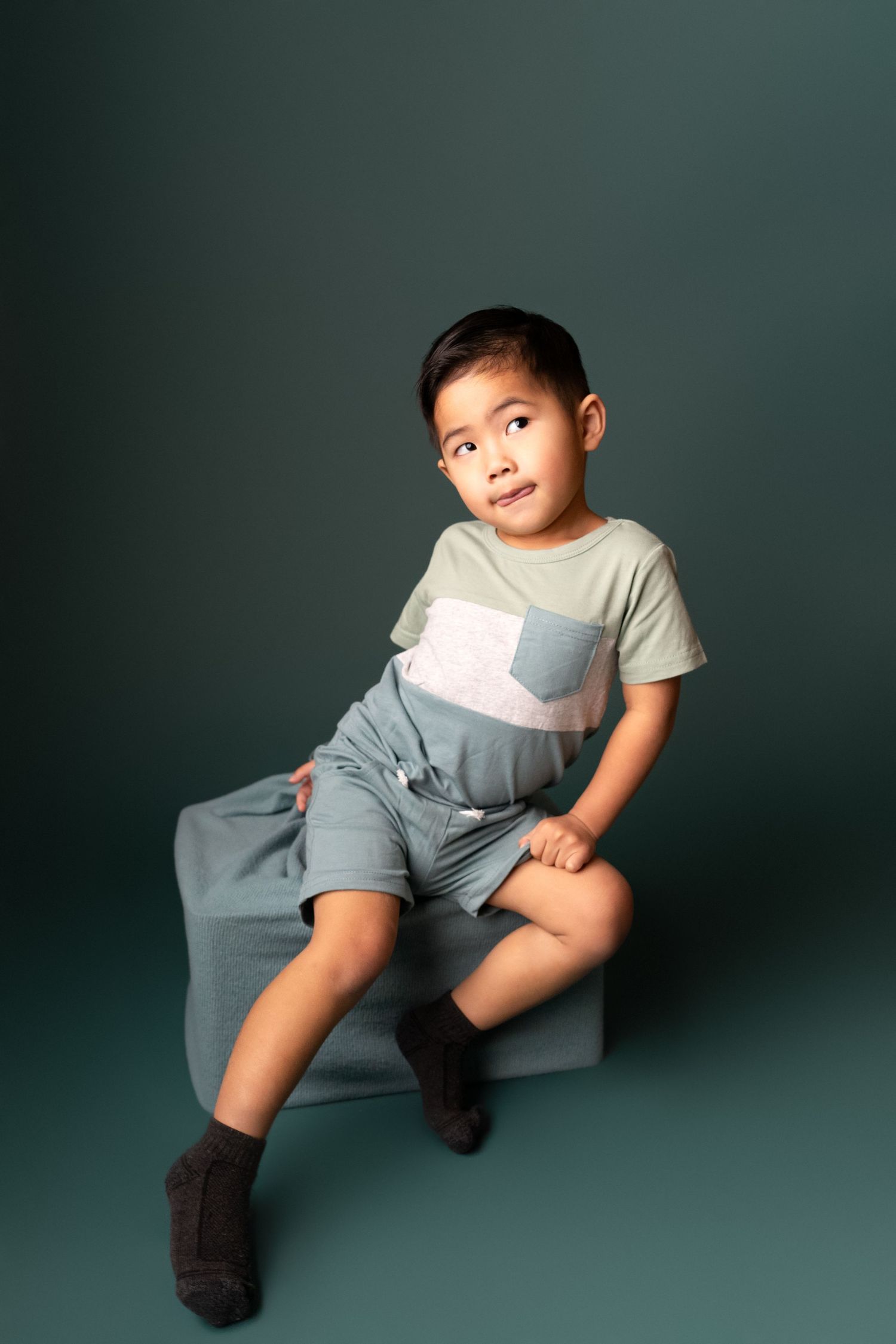 Casual poses on the floor wearing grey clothing against a dark teal backdrop.