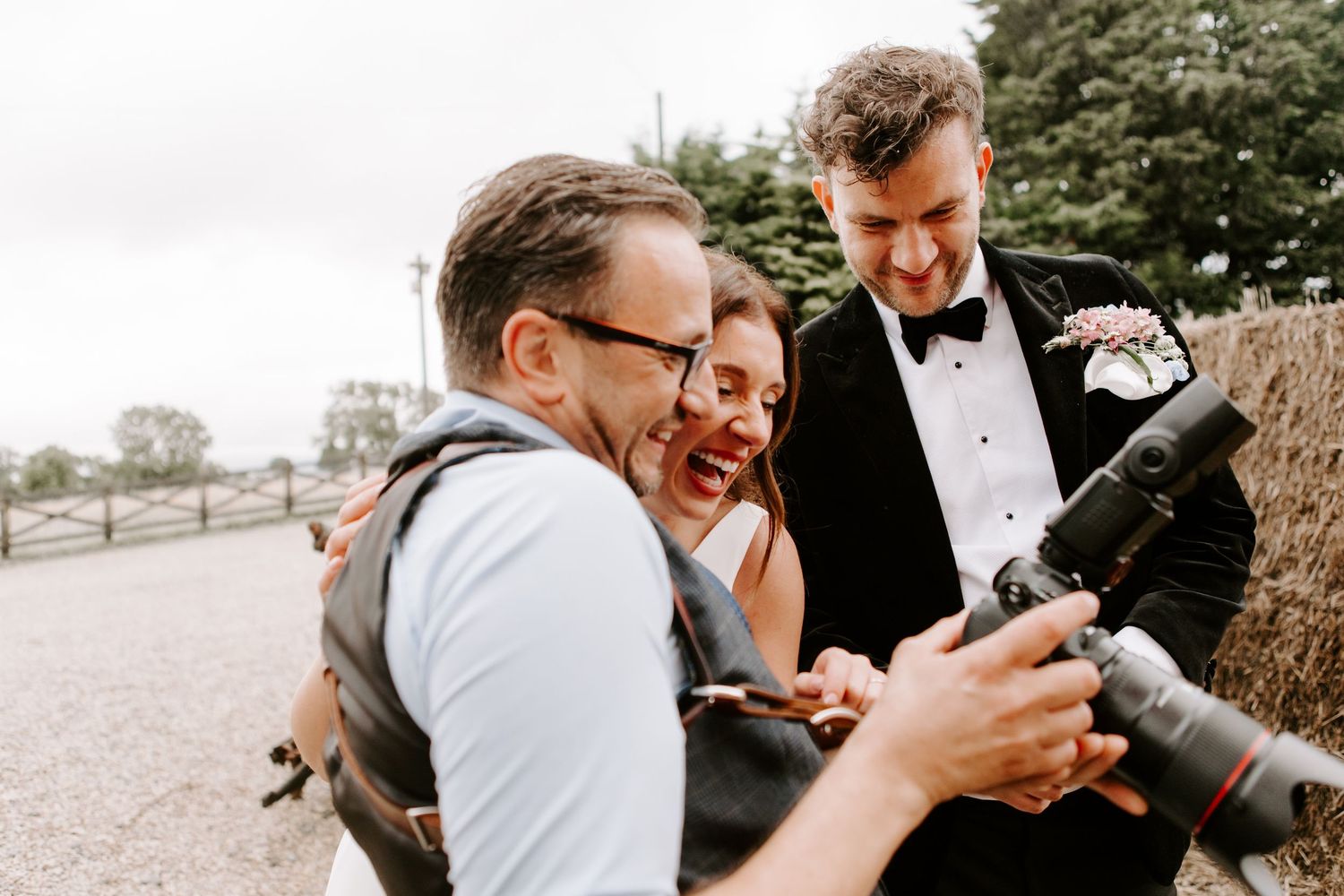Happy couple shares an intimate moment while looking at their phones during outdoor wedding photoshoot.