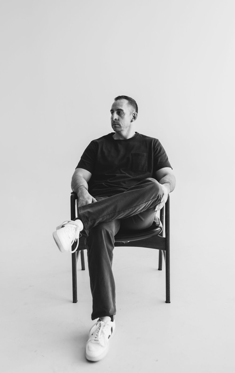 Minimalist black and white photo series showing someone seated in a chair against white background wearing dark clothing.