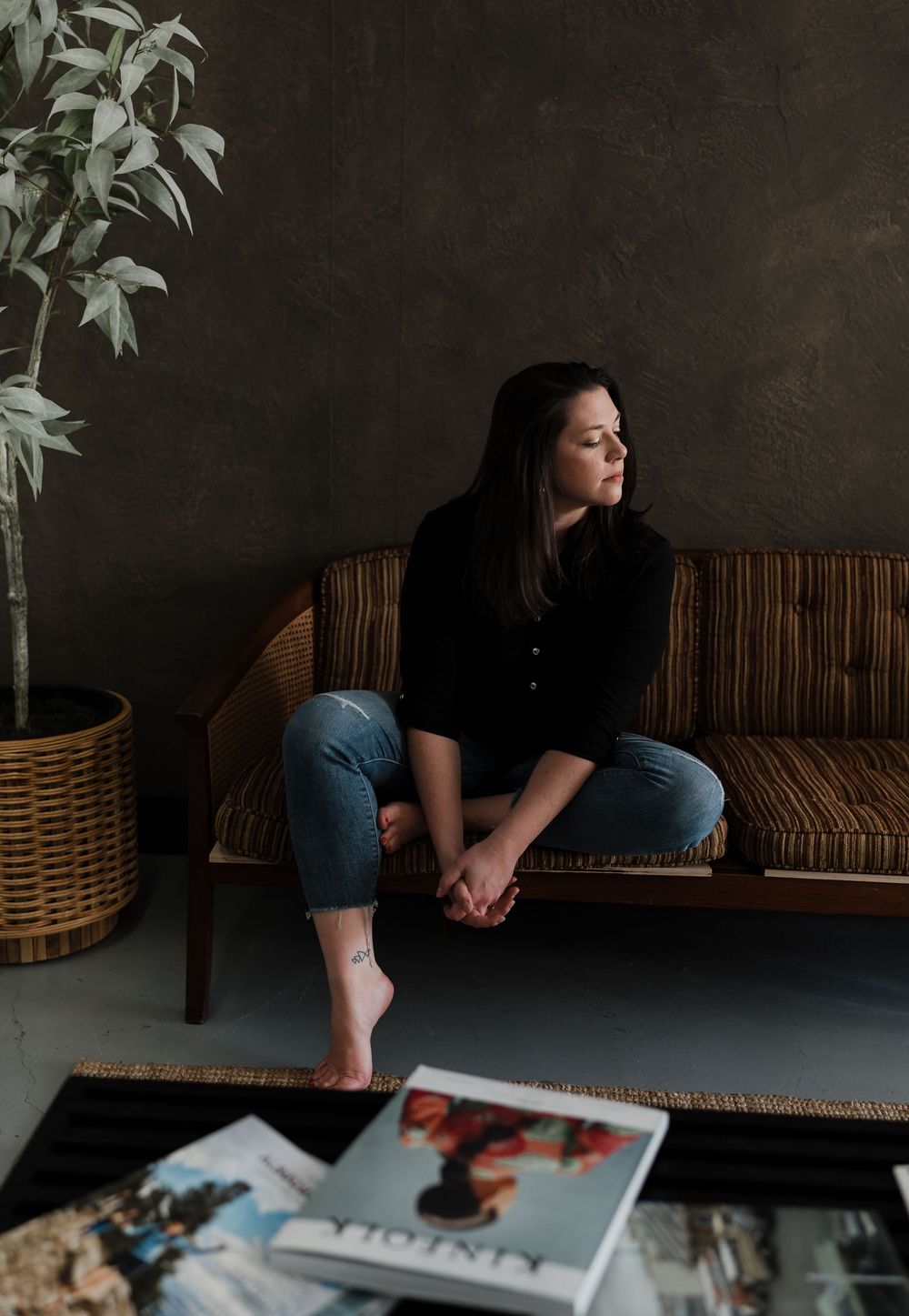 A moody indoor scene with a dark backdrop showing someone lounging on a rattan bench with magazines nearby.