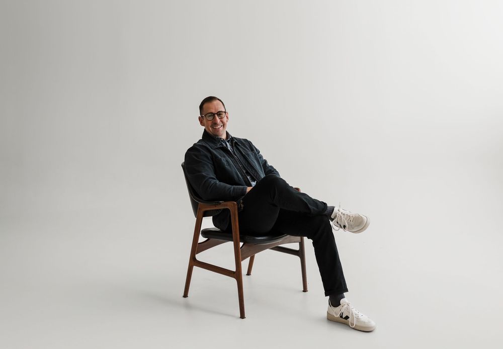 A figure sits in a wooden chair in various positions against a white studio background.