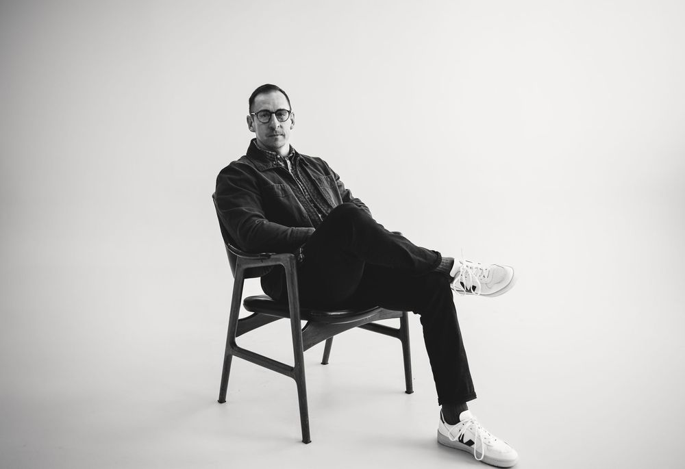 Minimalist black and white portrait series showing a figure seated on a chair against a white backdrop.