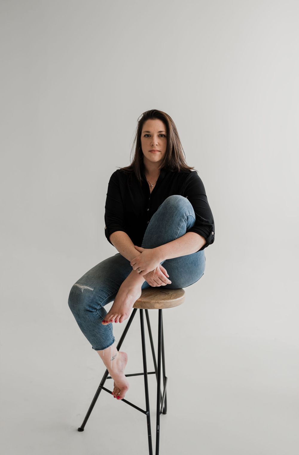 Series of artistic poses showing a person in black top and jeans sitting on a dark stool against white background.