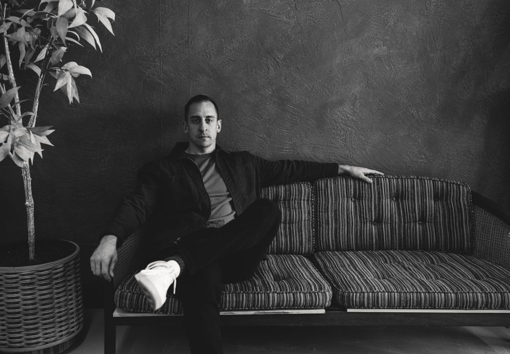 Black and white photos of a dark couch against textured wall with dramatic lighting and plant shadows.