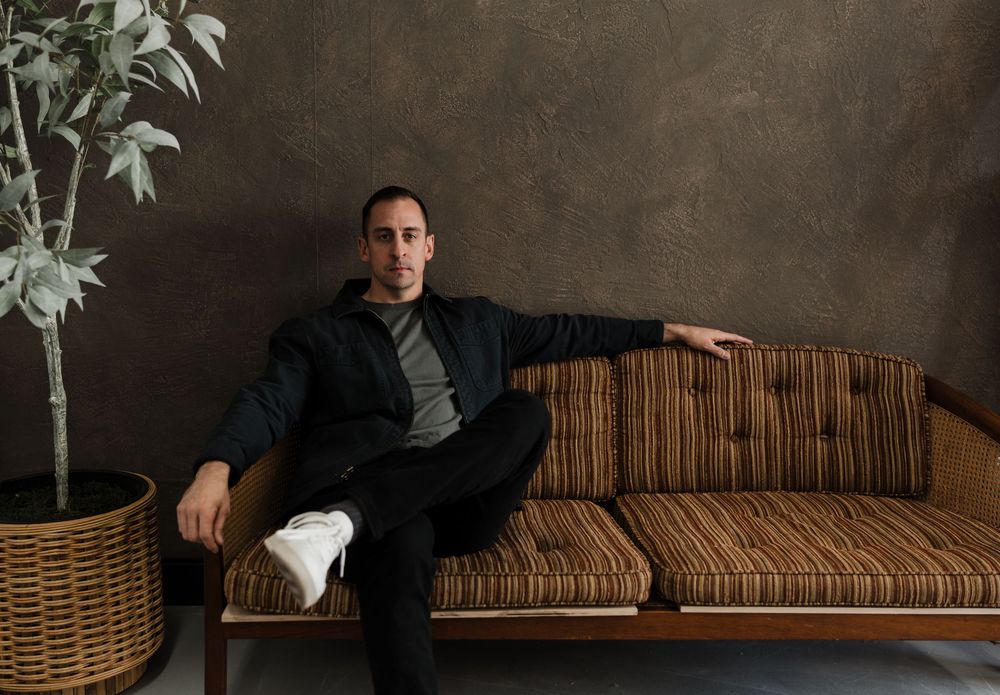 Person relaxing on striped vintage couch with potted plant beside dark textured wall.