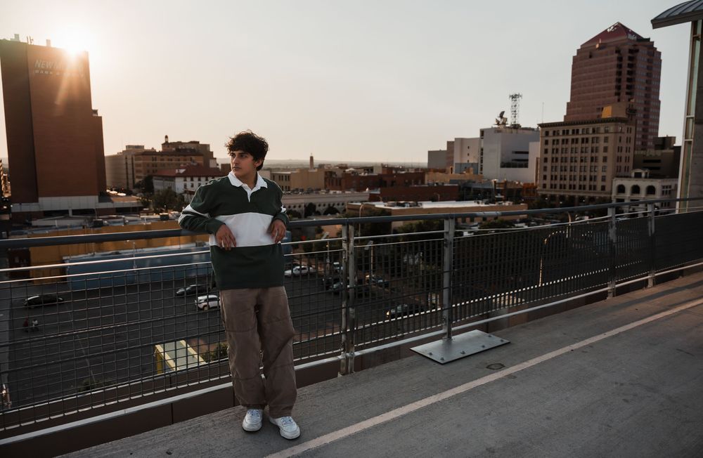Person walking on elevated walkway during golden sunset with urban skyline in background.