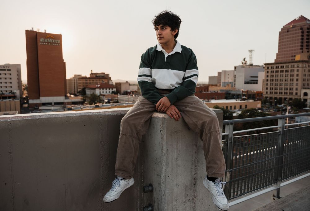 Person in a striped sweater sits on a concrete ledge overlooking an urban cityscape at dusk.