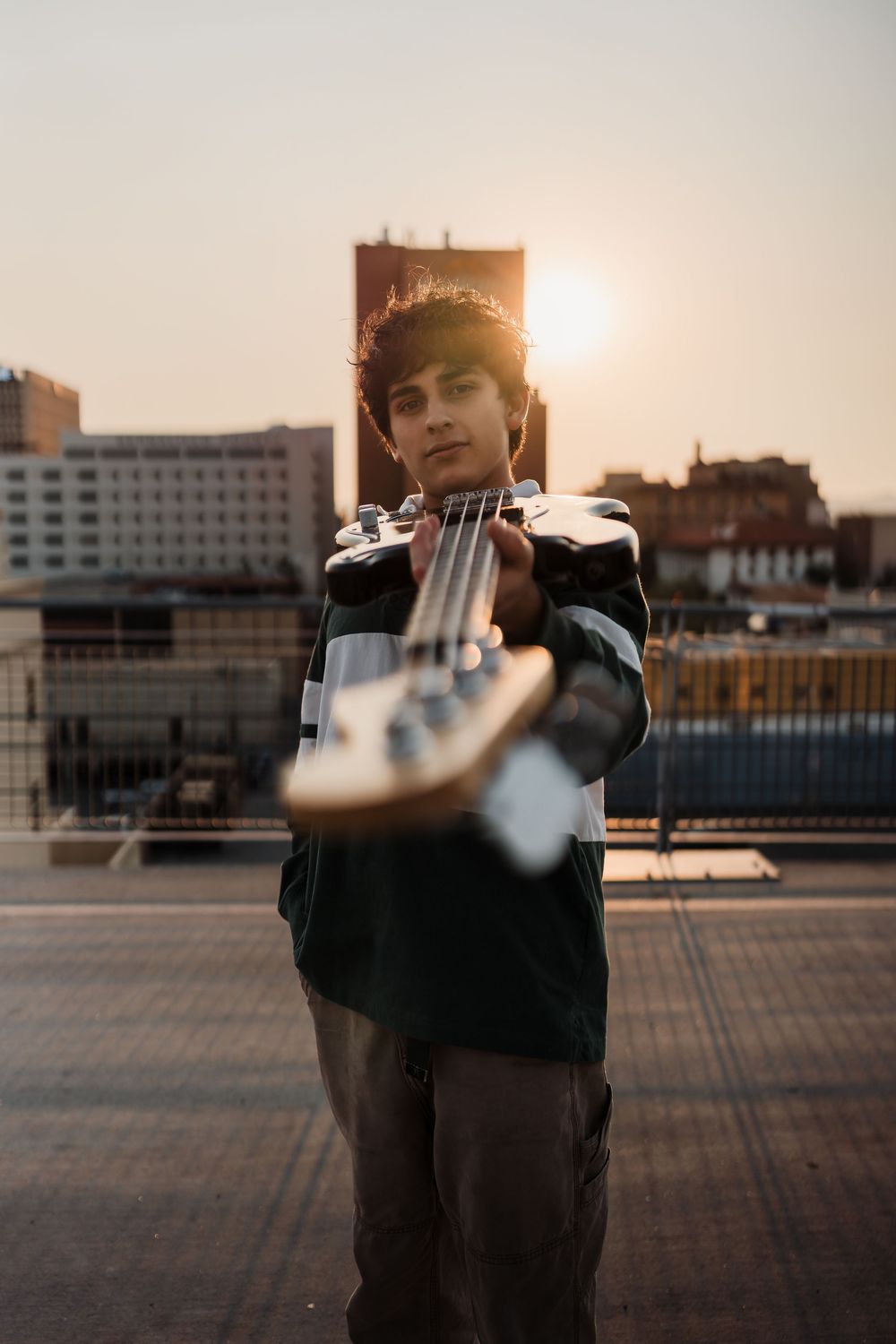 Silhouetted figure poses against warm sunset sky on urban rooftop with buildings visible in background.