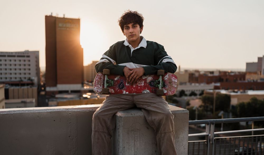 Person sits on rooftop ledge at sunset with city buildings in background and warm golden lighting.