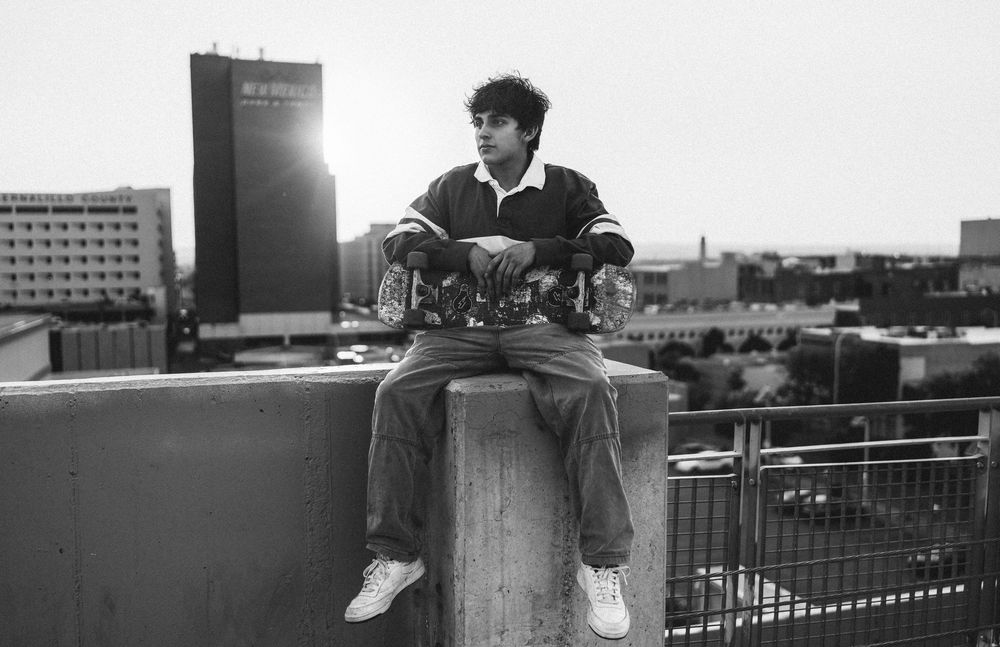 A black and white photo sequence shows someone sitting on a rooftop ledge overlooking an urban cityscape.
