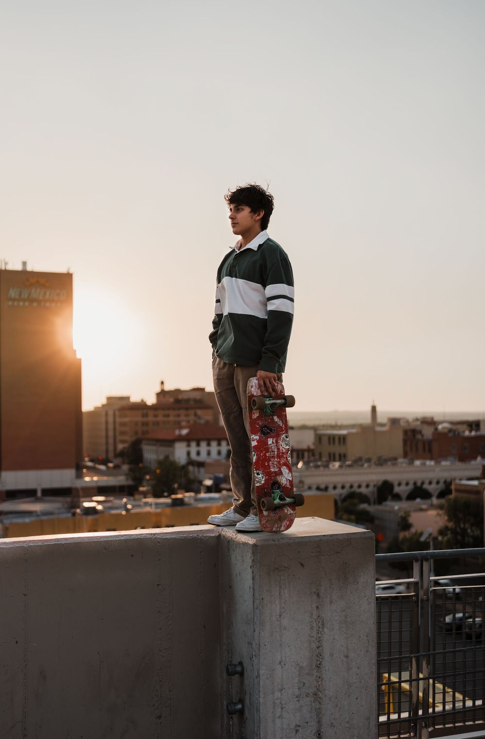 Person relaxes on concrete ledge during golden hour with cityscape behind them.