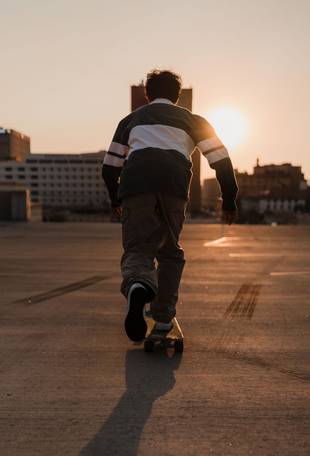 A person kneeling on a rooftop at sunset casting a long shadow across the concrete surface.